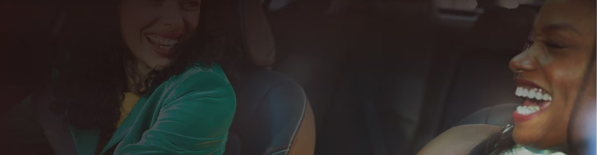 Two women laughing together while sitting in the front seats of a car.