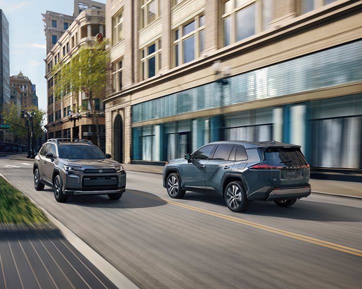 Un Toyota RAV4 gris et un Toyota Grand Highlander bleu circulent sur une rue de la ville.