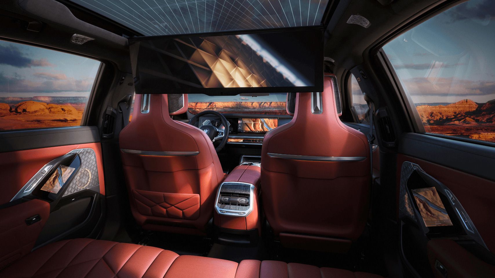 View of the rear cabin of a BMW 7 Series featuring red leather seats and the 31-inch BMW Theater Screen deployed from the ceiling.