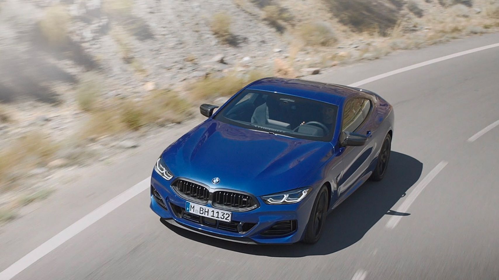 High-angle exterior view of a blue BMW 8 Series Coupe driving on a winding mountain road.
