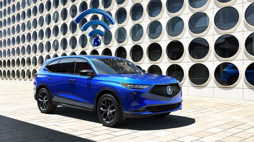 VUS Acura bleu avec une icône Wi-Fi au-dessus, stationné à côté d'un mur architectural blanc.