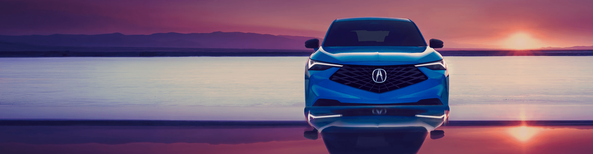 Front view of a blue Acura at sunset, reflected on a glossy surface against a purple mountain horizon.