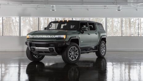 SUV GMC Hummer EV vert militaire stationné à l'intérieur d'un studio d'exposition lumineux avec de grandes fenêtres en arrière-plan.