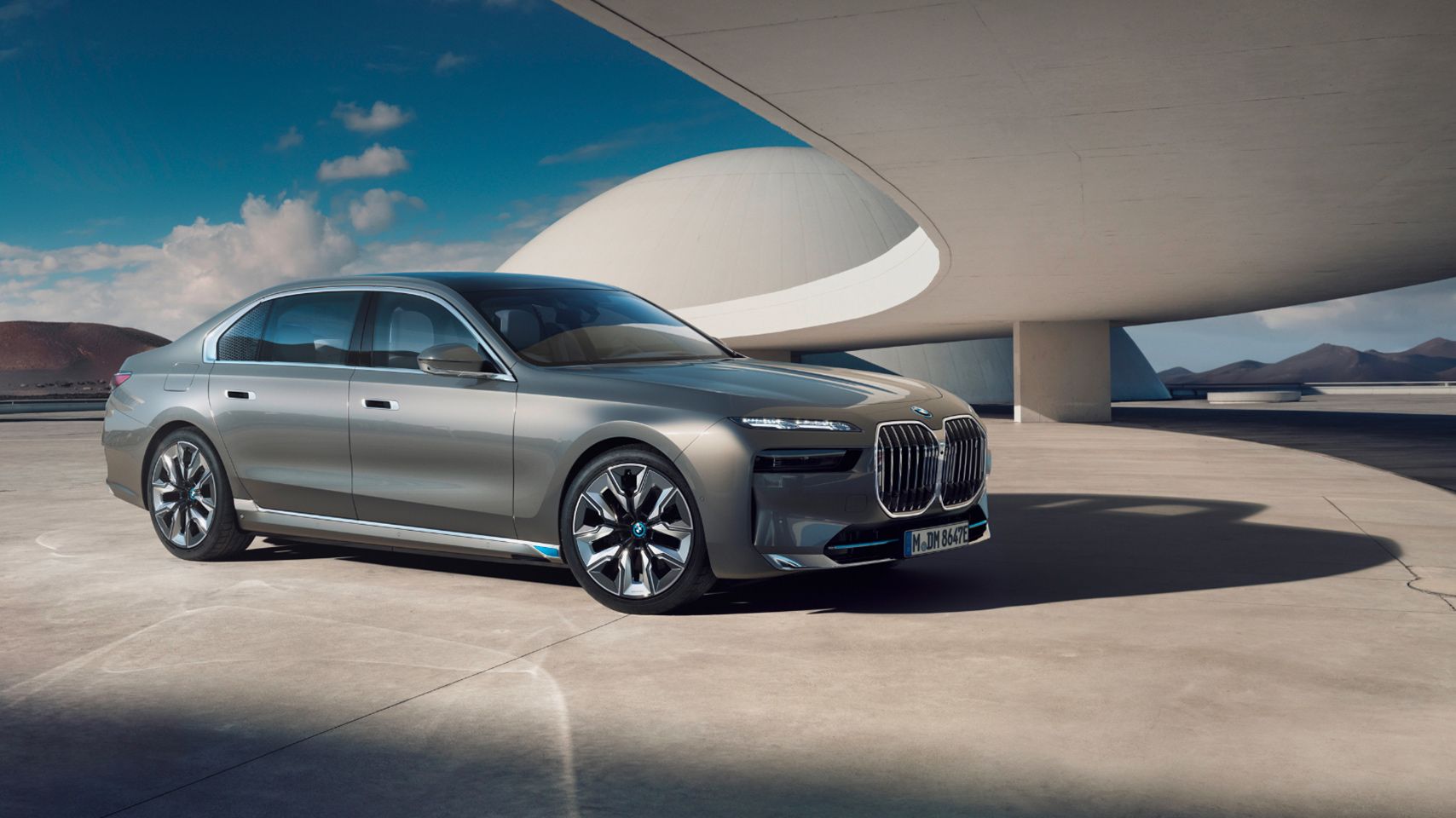 Front three-quarter exterior view of a silver BMW i7 sedan parked in a modern architectural setting.