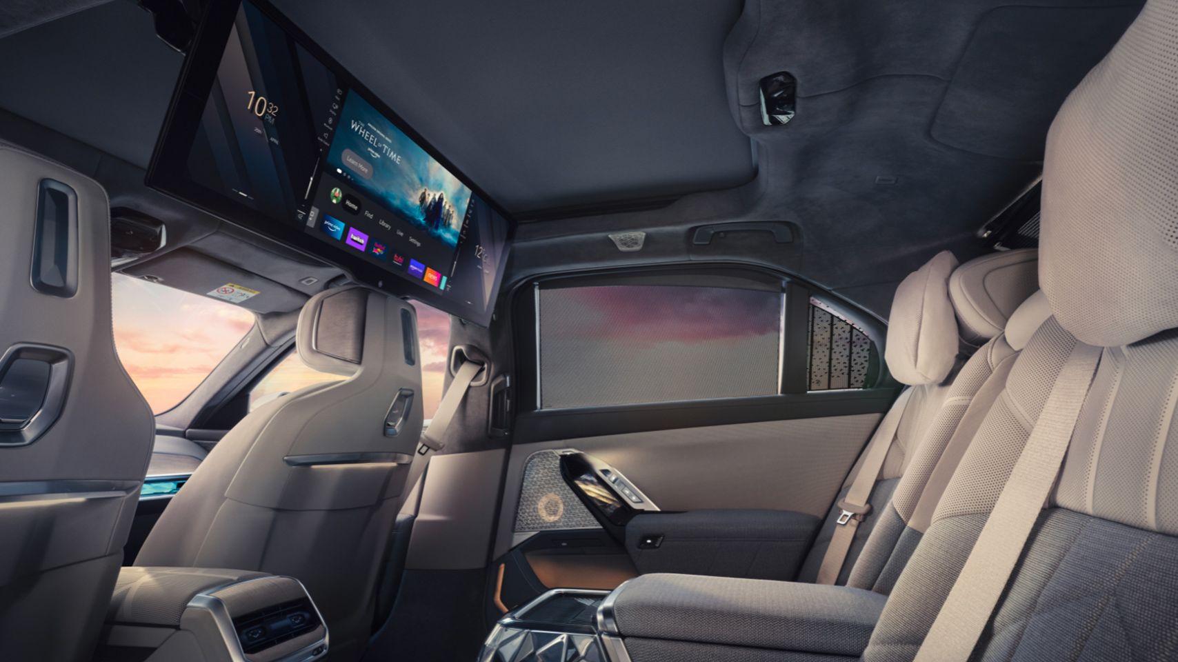 Rear passenger cabin of a BMW i7 showing the fold-down theater screen and luxury seating.
