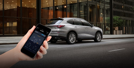 Personne tenant un téléphone avec l'application AcuraLink ouverte près d'un Acura MDX argenté en ville.