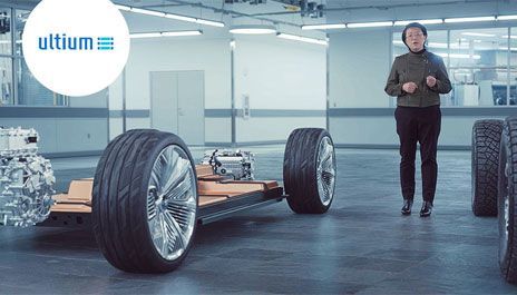 Une présentation de la plateforme de batterie électrique GM Ultium avec un châssis roulant exposant les roues et la batterie, et une présentatrice debout à droite.