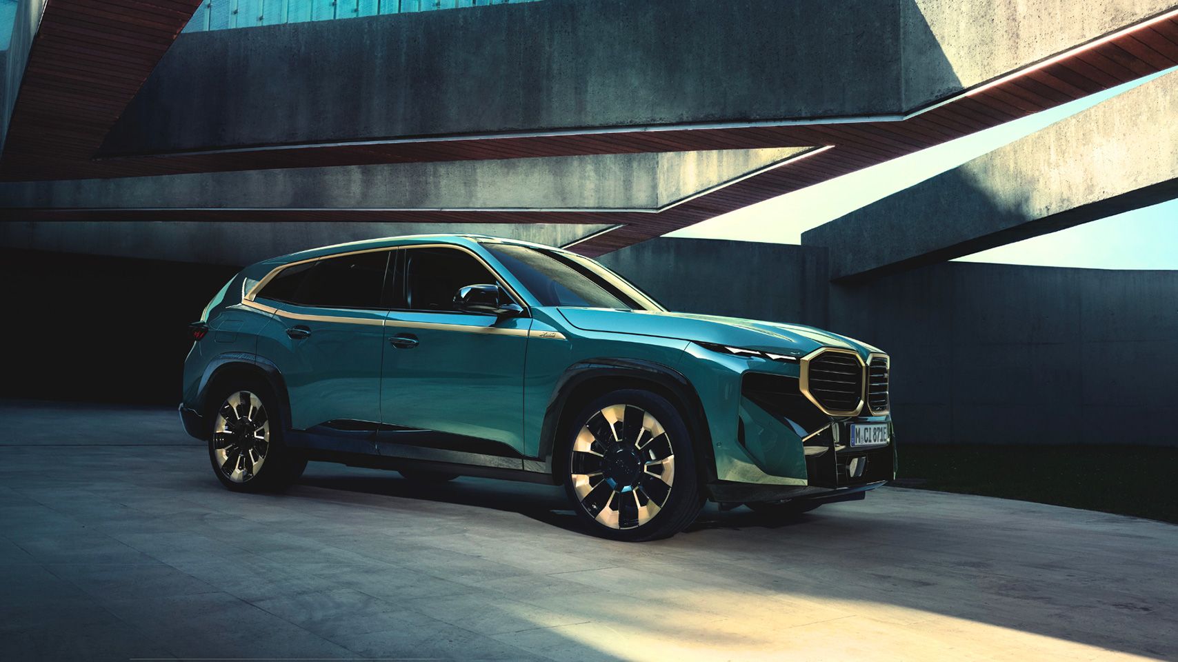 Side profile exterior view of a teal BMW XM SUV parked in a modern, angular concrete structure.