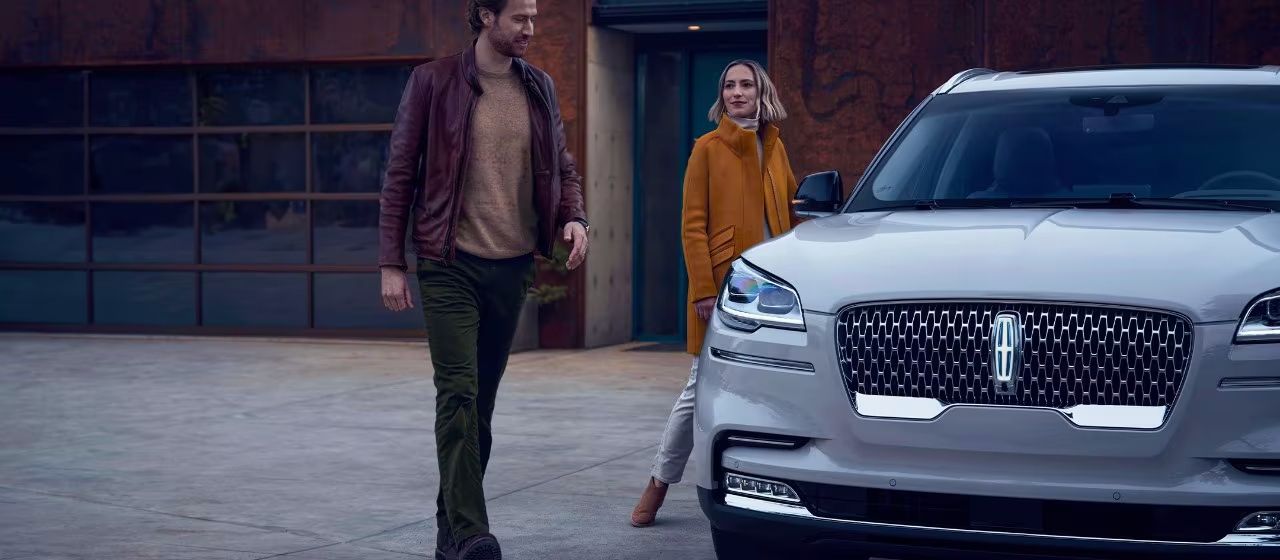 Couple walking toward a white Lincoln luxury SUV parked in front of a modern home