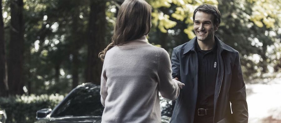 A smiling Lincoln concierge representative shaking hands with a customer in front of a vehicle