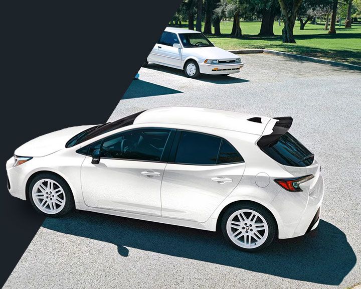 Vue latérale d'une Toyota Corolla Hatchback blanche avec un aileron arrière noir, garée dans un espace extérieur ensoleillé.