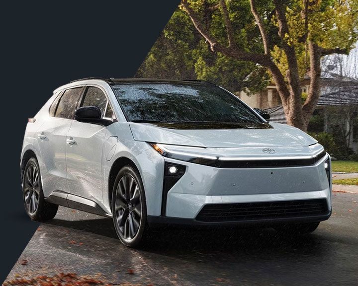 Vue de trois-quarts avant d'un Toyota bZ4X électrique blanc sous une lumière naturelle filtrée par des arbres.