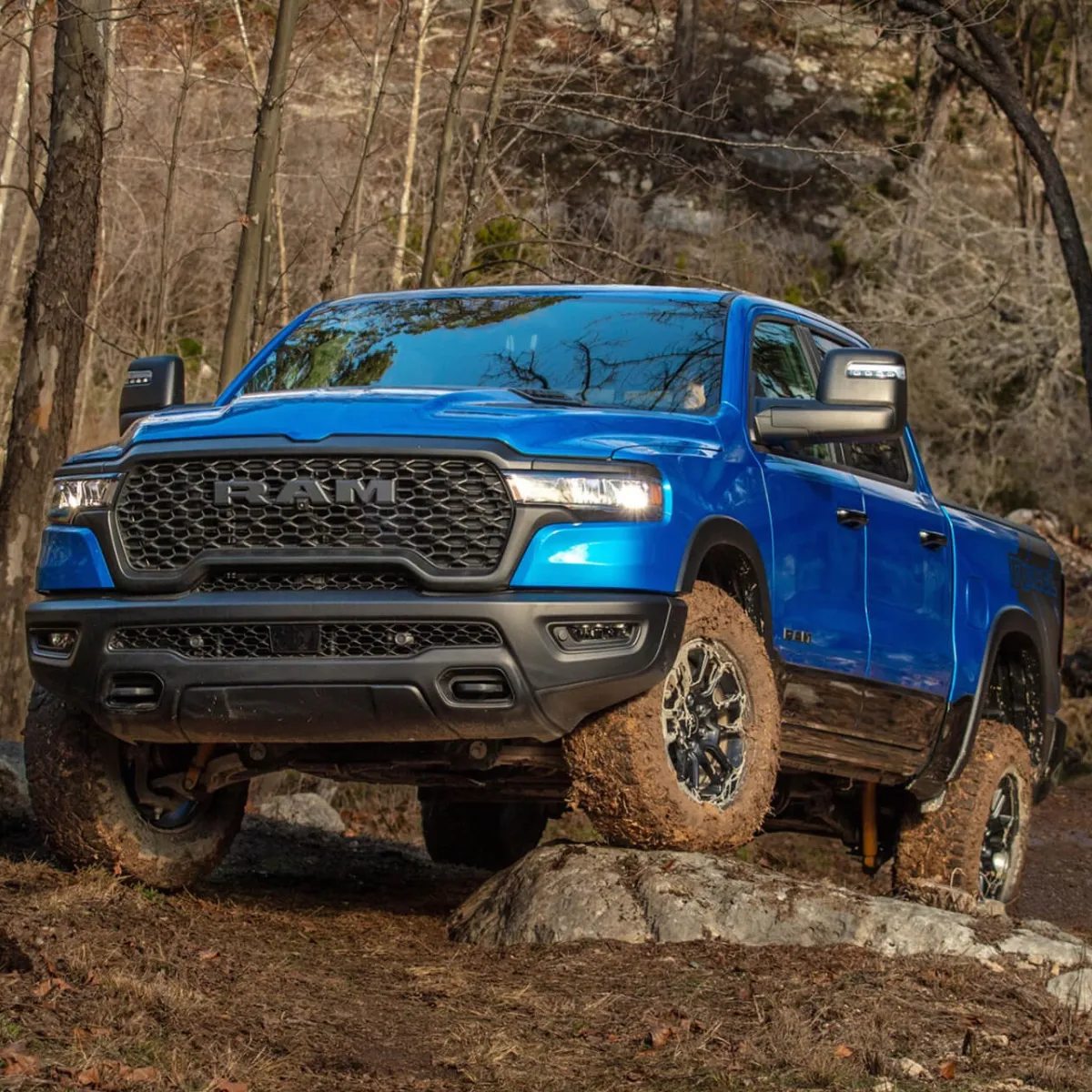 Ram 1500 2027 bleu couvert de boue sur un rocher, en forêt.