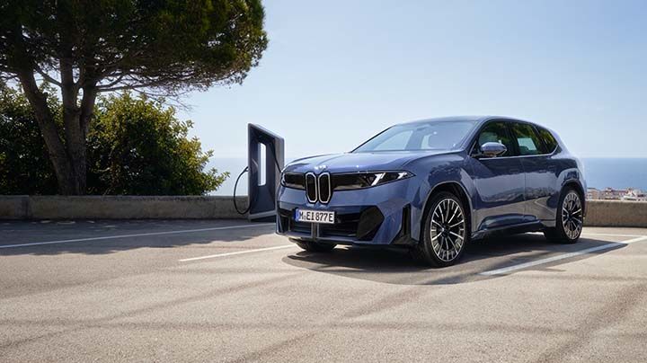 Un SUV BMW X7 gris garé au bord d'une piscine à débordement, portière arrière ouverte, sur fond de paysage montagneux.