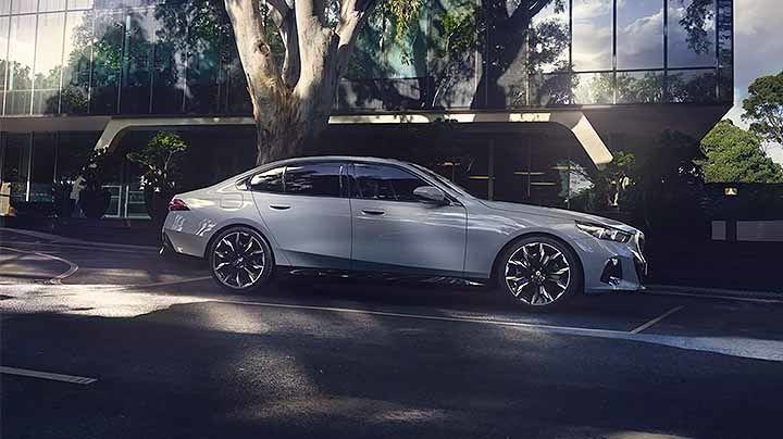 Side profile of a blue metallic BMW 7 Series sedan parked on a rocky surface at sunset.