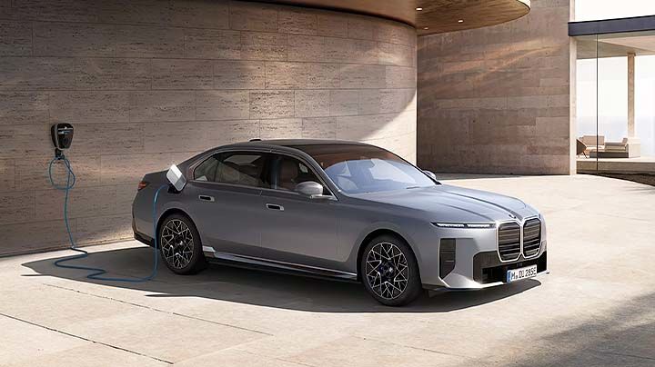Vue trois quarts avant d'une berline électrique de luxe BMW i7 gris métallique stationnée devant une architecture moderne.