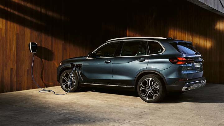 Vue en plongée de l'extérieur d'un SUV BMW X7 gris stationné près d'un bassin réfléchissant, portière arrière ouverte.