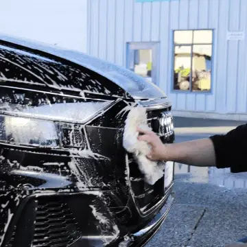 Hand washing the soapy front grille of a black car.
