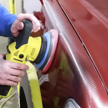 Buffing and polishing a red car's paint with a rotary polisher.