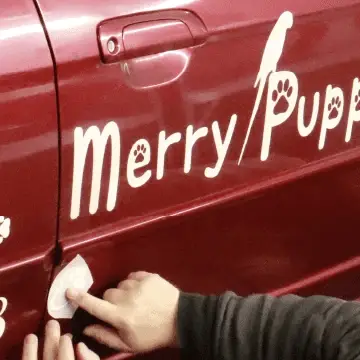 Applying a custom vinyl decal onto a red car door.