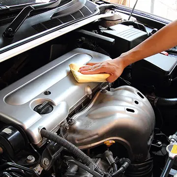 Hand cleaning and detailing a car's engine bay.