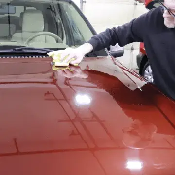 Applying hand wax to the shiny hood of a red vehicle.