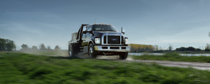 Camion commercial Ford châssis-cabine noir roulant sur un chemin de campagne.