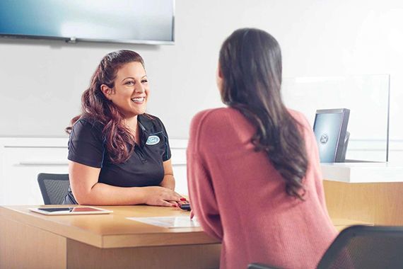 A smiling dealership representative in a uniform sitting across a desk and speaking with a customer