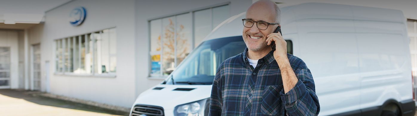 Homme d'affaires souriant au téléphone devant un fourgon commercial Ford blanc.