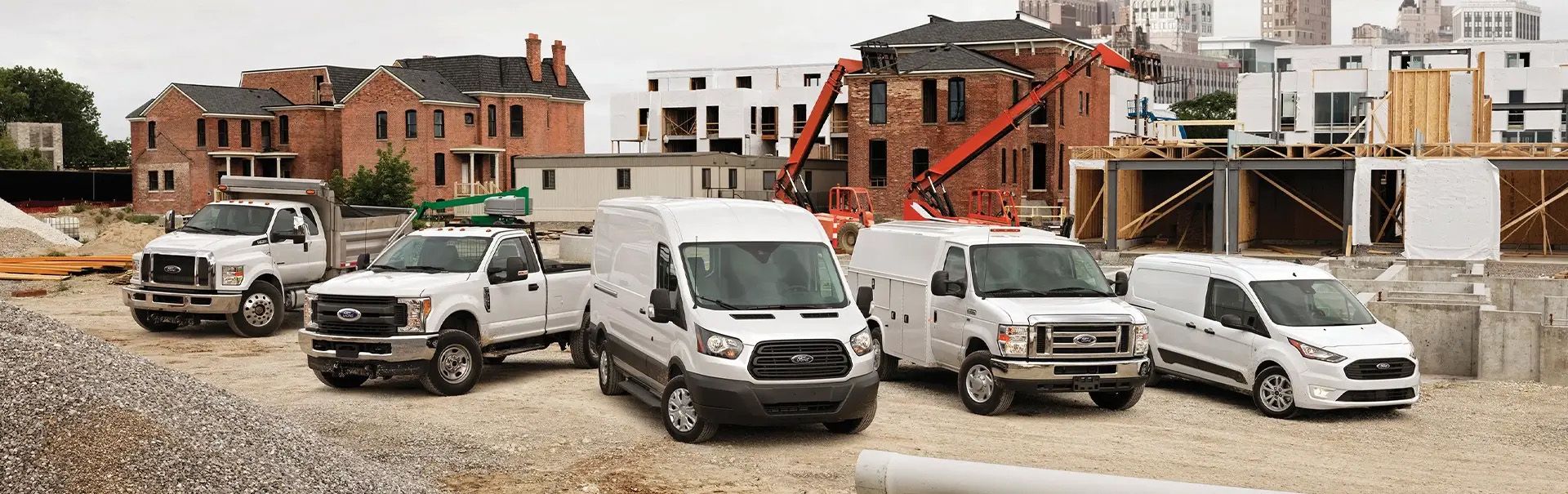 Gamme de camions et fourgons commerciaux Ford blancs stationnés sur un chantier de construction.