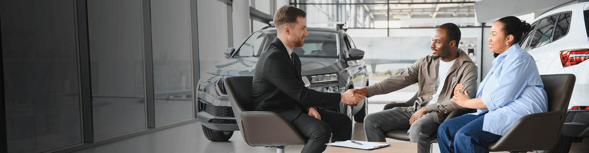 Salesman shaking hands with a couple in a car dealership.
