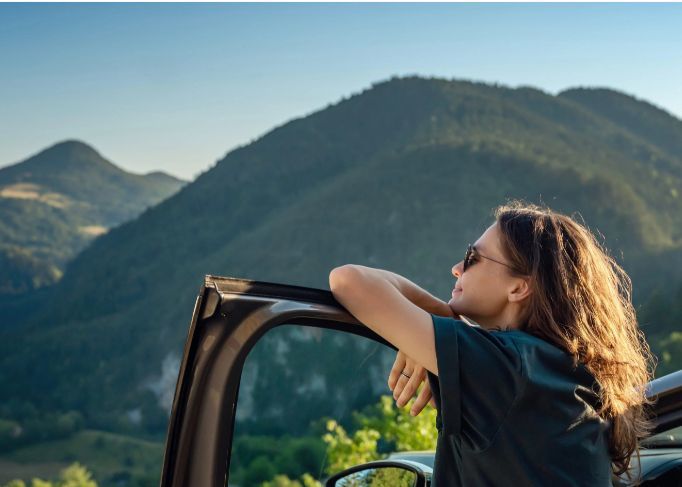 Homme souriant portant une veste rouge, debout dans un concessionnaire automobile.