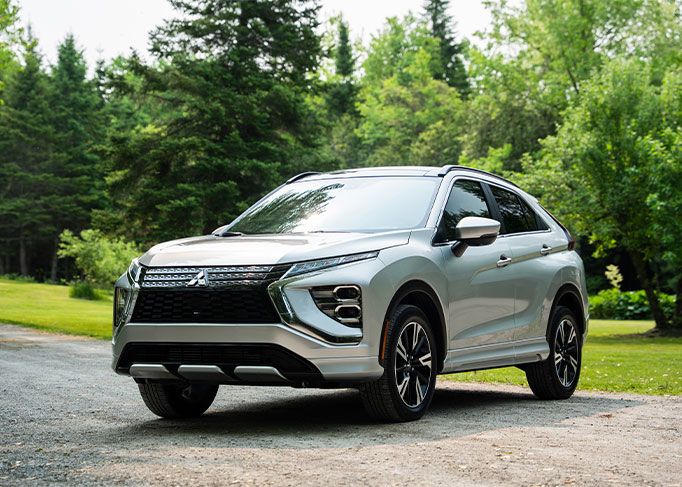 A red sedan is parked on a mountain road, with a large rocky cliff in the background.