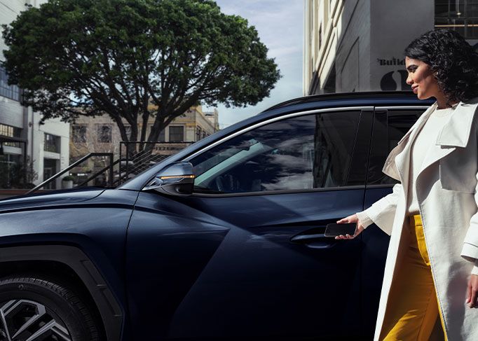 A smiling man sits in the driver's seat of a modern car, looking at his smartphone.