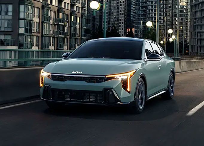 A red sedan is parked on a mountain road, with a large rocky cliff in the background.