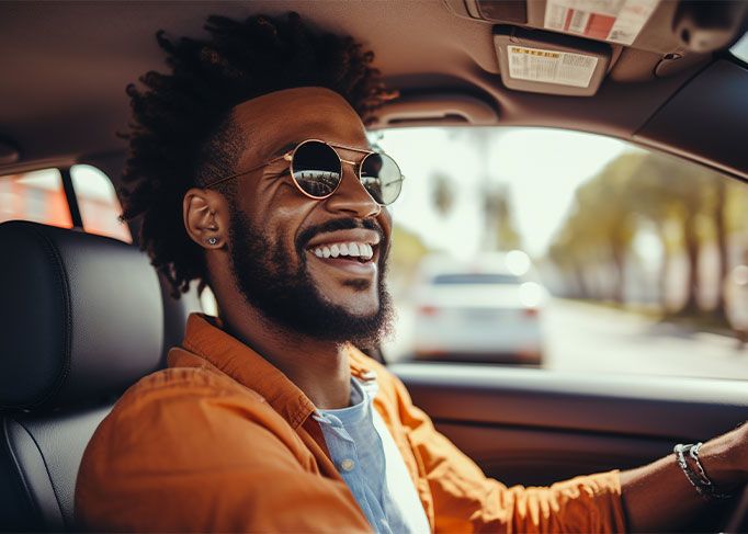 A smiling man sits in the driver's seat of a modern car, looking at his smartphone.