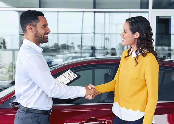 A smiling man sits in the driver's seat of a modern car, looking at his smartphone.