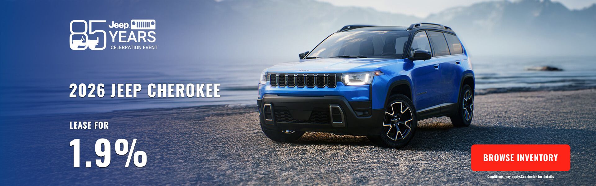 Blue 2026 Jeep Cherokee SUV parked on a lakeside beach.