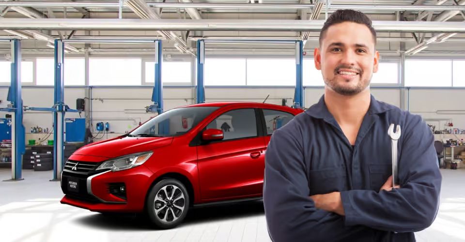 Smiling mechanic holding a wrench in front of a red Mitsubishi car in an auto shop.