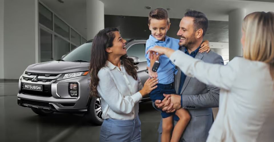 Happy family receiving new Mitsubishi SUV keys at a dealership.