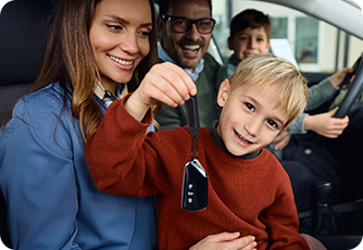 Young boy holding a car key inside a vehicle with his happy family.