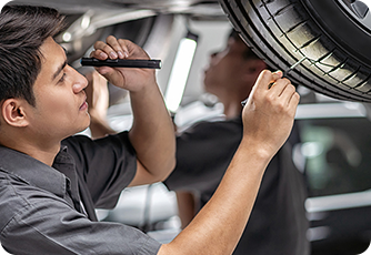 Mechanic inspecting the underside of a car and tires with a flashlight.