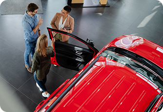 High angle view of a couple talking to a sales representative beside a red car.