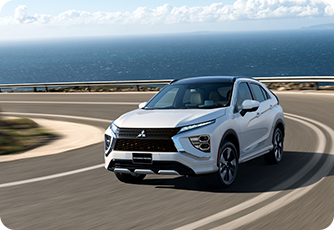 White Mitsubishi SUV driving on a winding coastal road along the ocean.