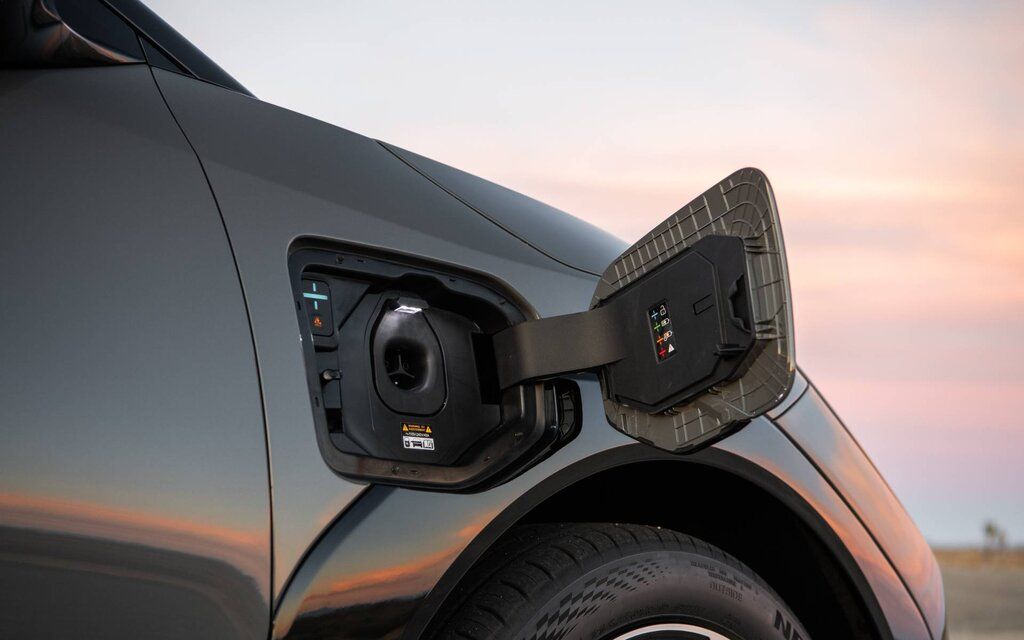 A red sedan is parked on a mountain road, with a large rocky cliff in the background.