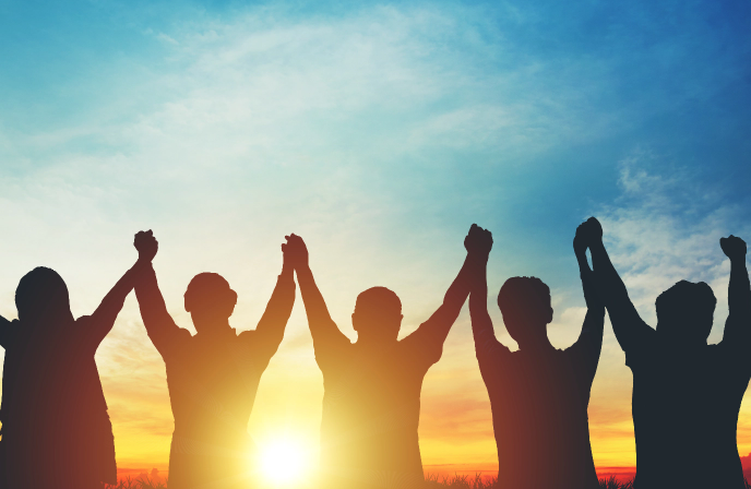 A silhouette of five people standing in a row against a vibrant sunrise or sunset, holding their joined hands high in the air in a gesture of unity and triumph.