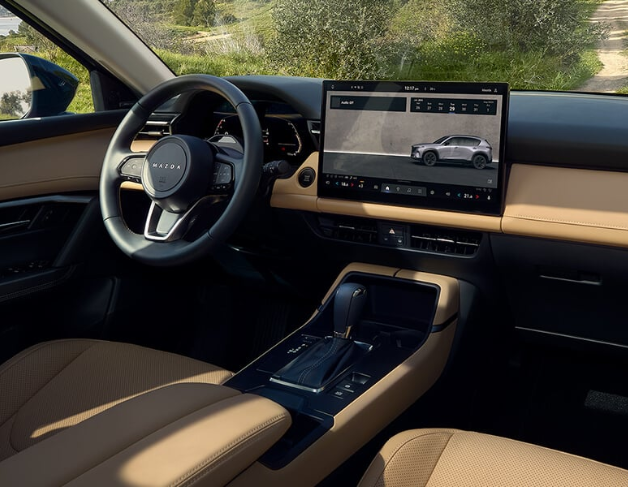 A red sedan is parked on a mountain road, with a large rocky cliff in the background.