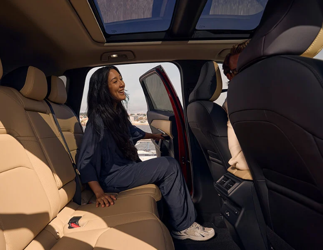 A smiling man sits in the driver's seat of a modern car, looking at his smartphone.