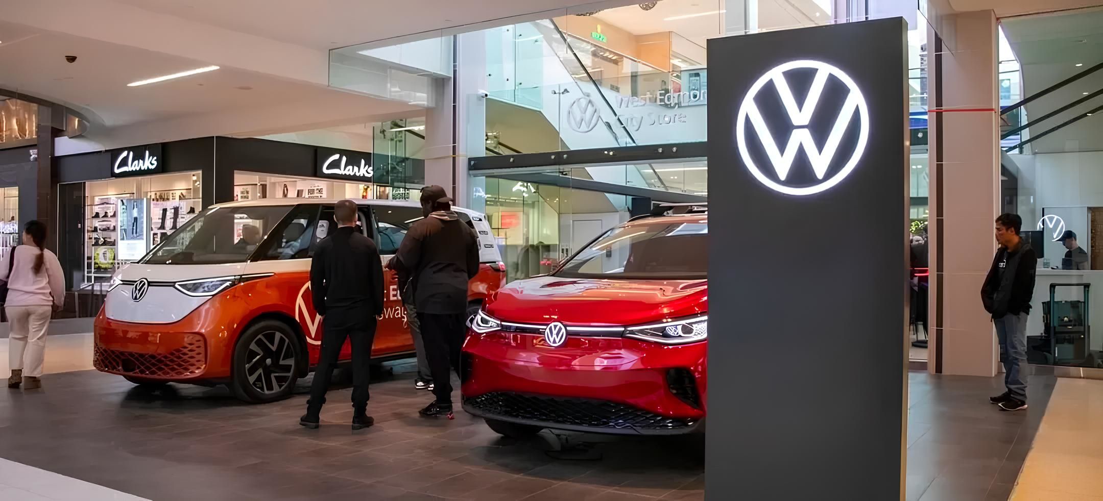 A street-level view featuring a bold red ID.4 and an orange/white ID. Buzz parked next to a large, glowing Volkswagen monolith.