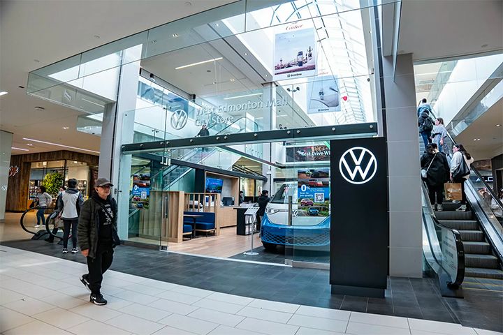A wide exterior shot showing the store's glass facade and main entrance, located directly next to a mall escalator.